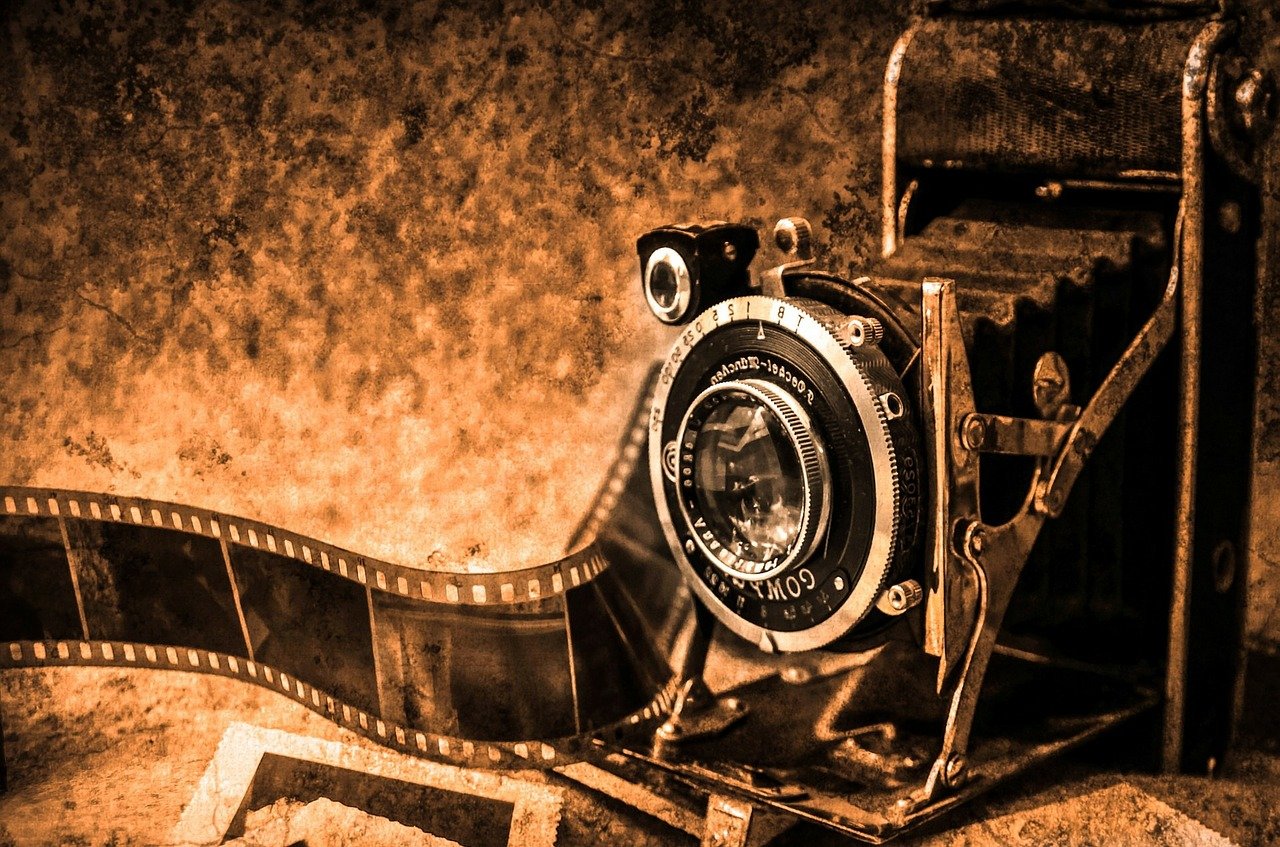 Grafika przedstawiająca stary aparat fotograficzny wraz z kliszą. Całość w odcieniach sepii.